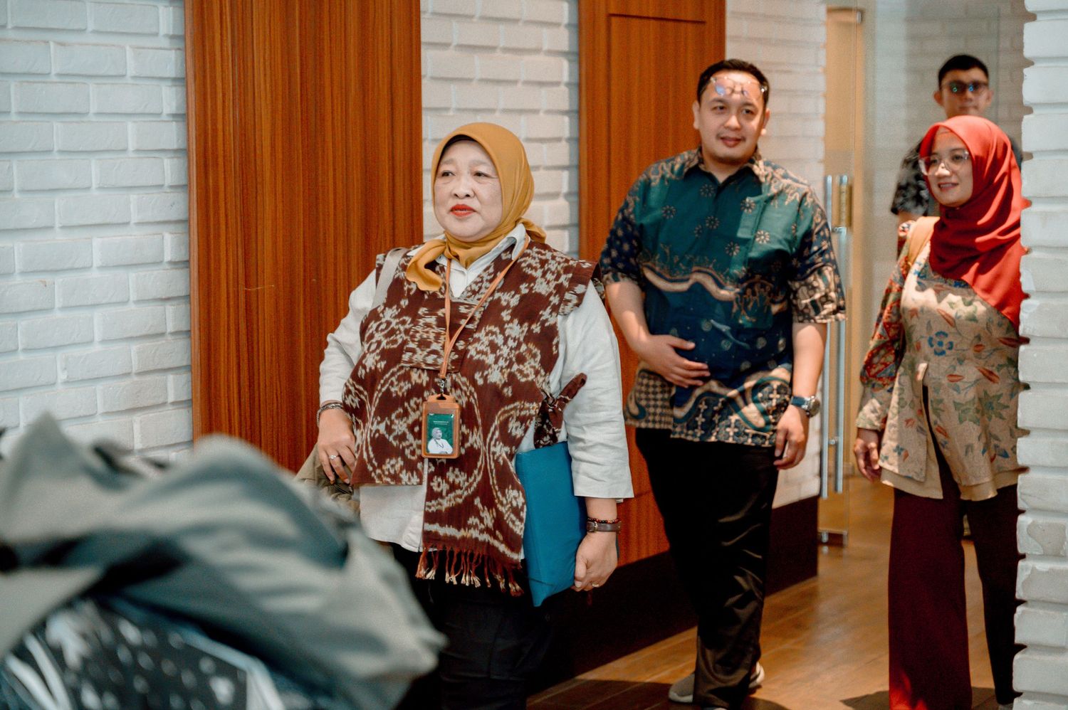 Group of people wearing traditional Indonesian batik attire walking indoors near a brick wall.