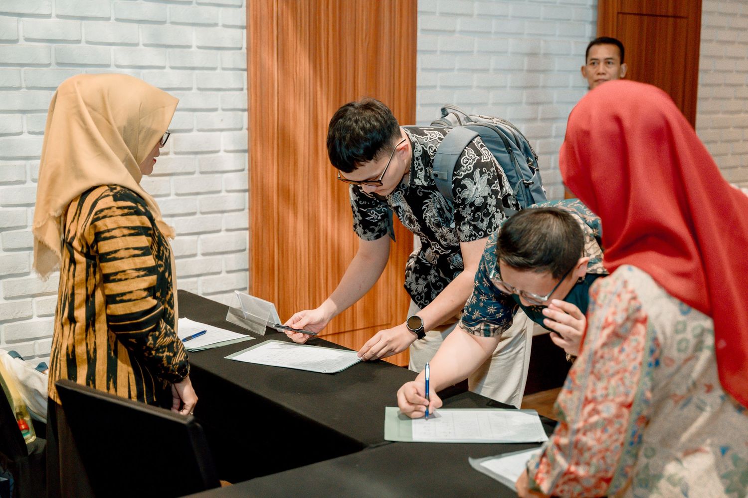 People in batik attire signing documents at a formal meeting table in an indoor setting.