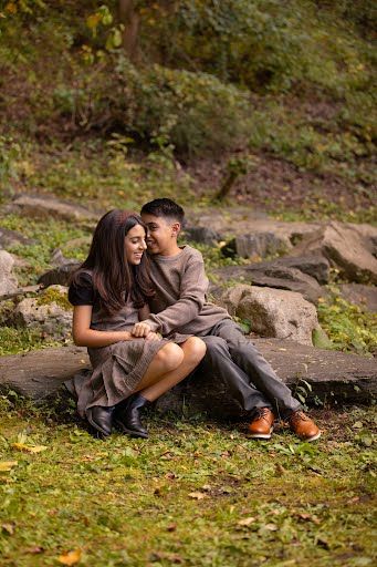 A young couple sits closely together on a rock in an autumn park, wearing matching brown outfits and leather shoes.