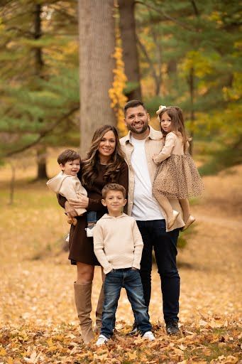 Family of five posing outdoors in autumn park surrounded by colorful fall foliage for a seasonal portrait.
