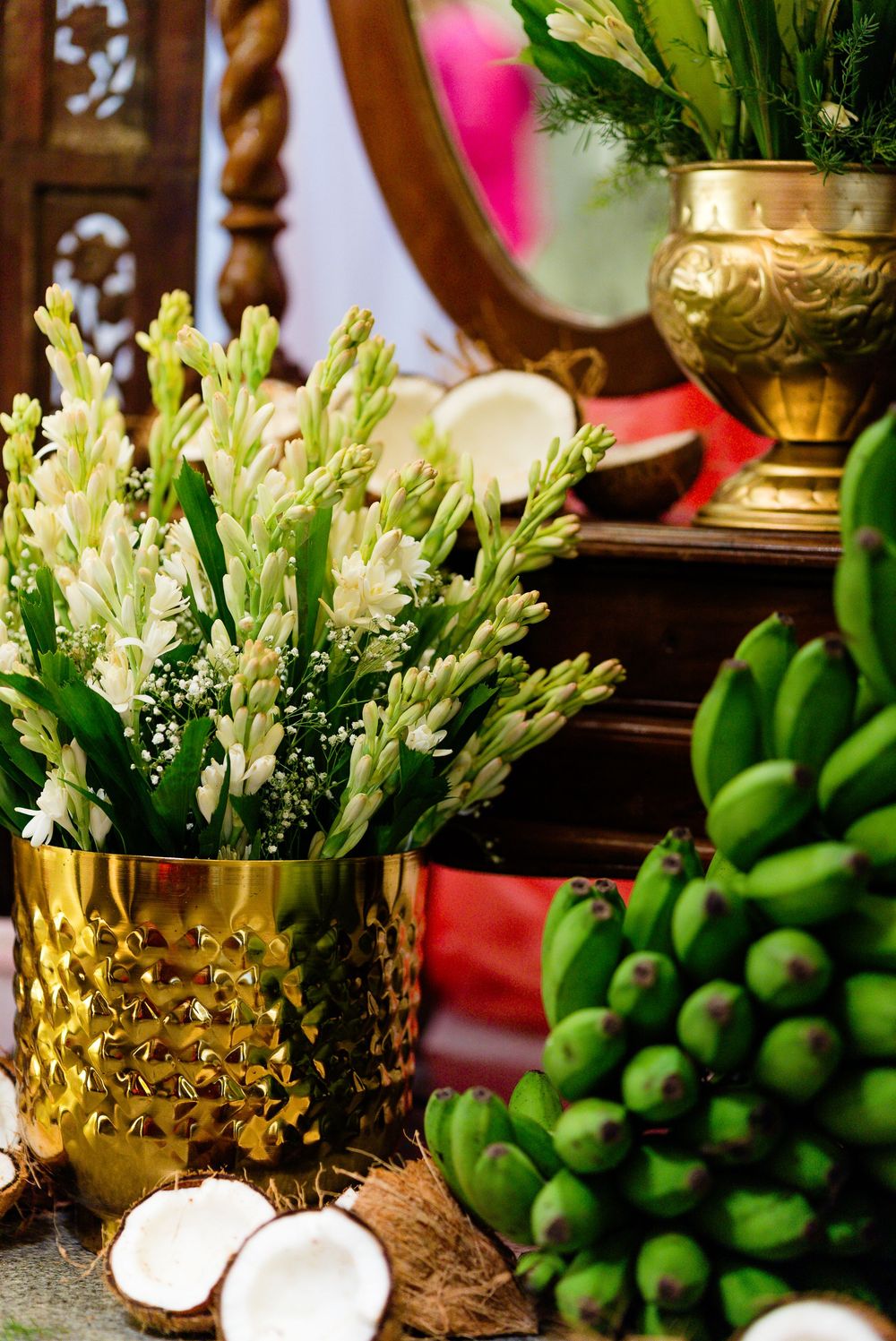 Gold vases with white tuberose flowers, green bananas, and coconuts arranged for a traditional Hindu puja ceremony.