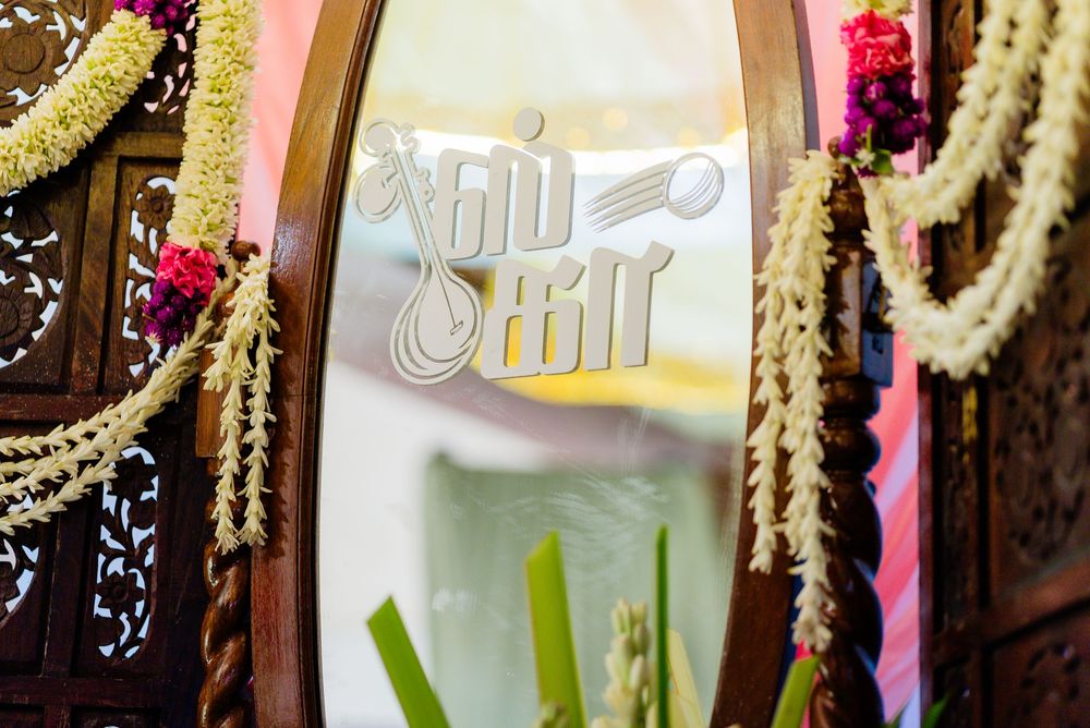 Decorative wooden mirror with Tamil script lettering, adorned with jasmine garlands at a South Indian wedding.