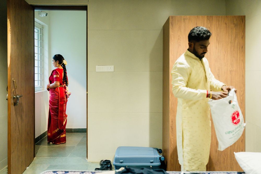 Indian bride in red saree and groom in cream sherwani preparing separately in a modern room before wedding.