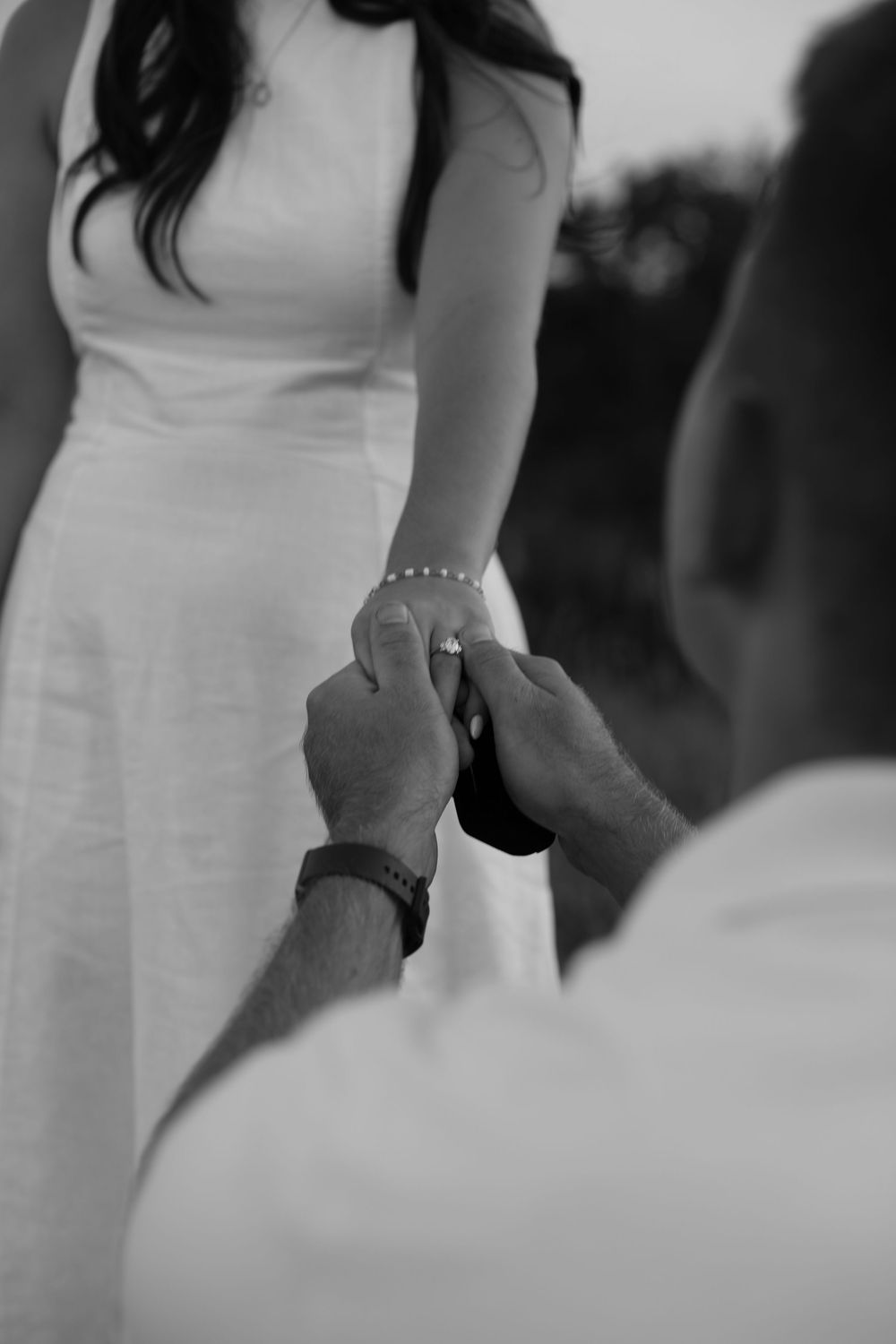 Black and white photo of a man placing an engagement ring on a womans finger during a romantic proposal.