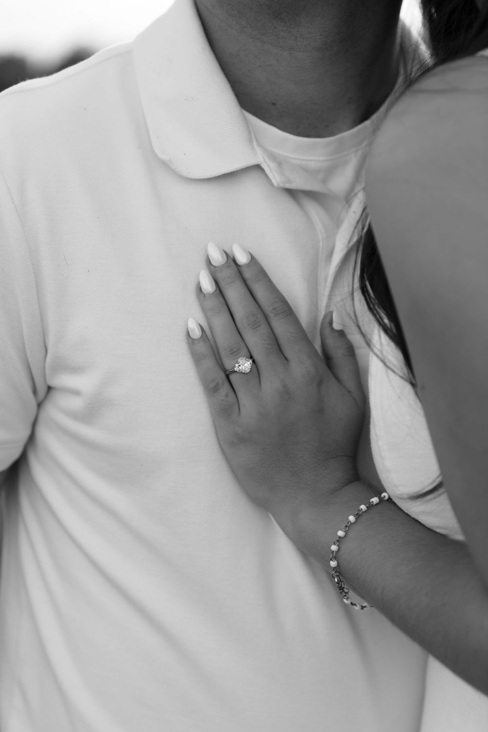 Black and white photo of a woman's hand with engagement ring and bracelet resting on a man's chest.