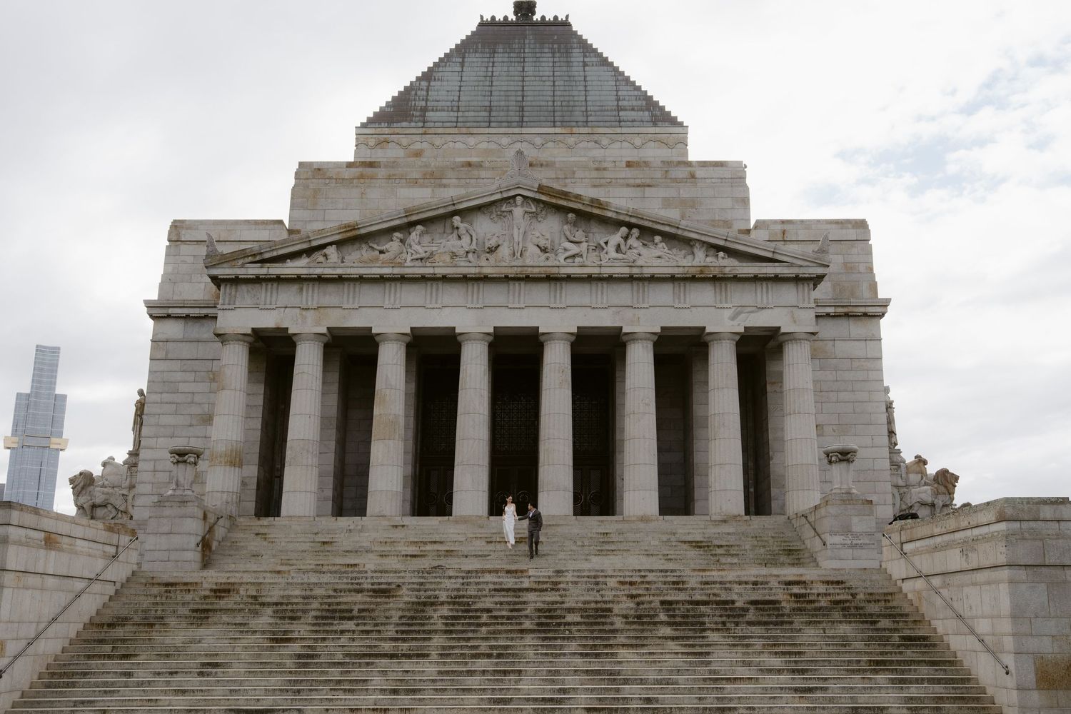 Couple in wedding attire standing on steps of the Shrine of Remembrance in Melbourne, Australia.