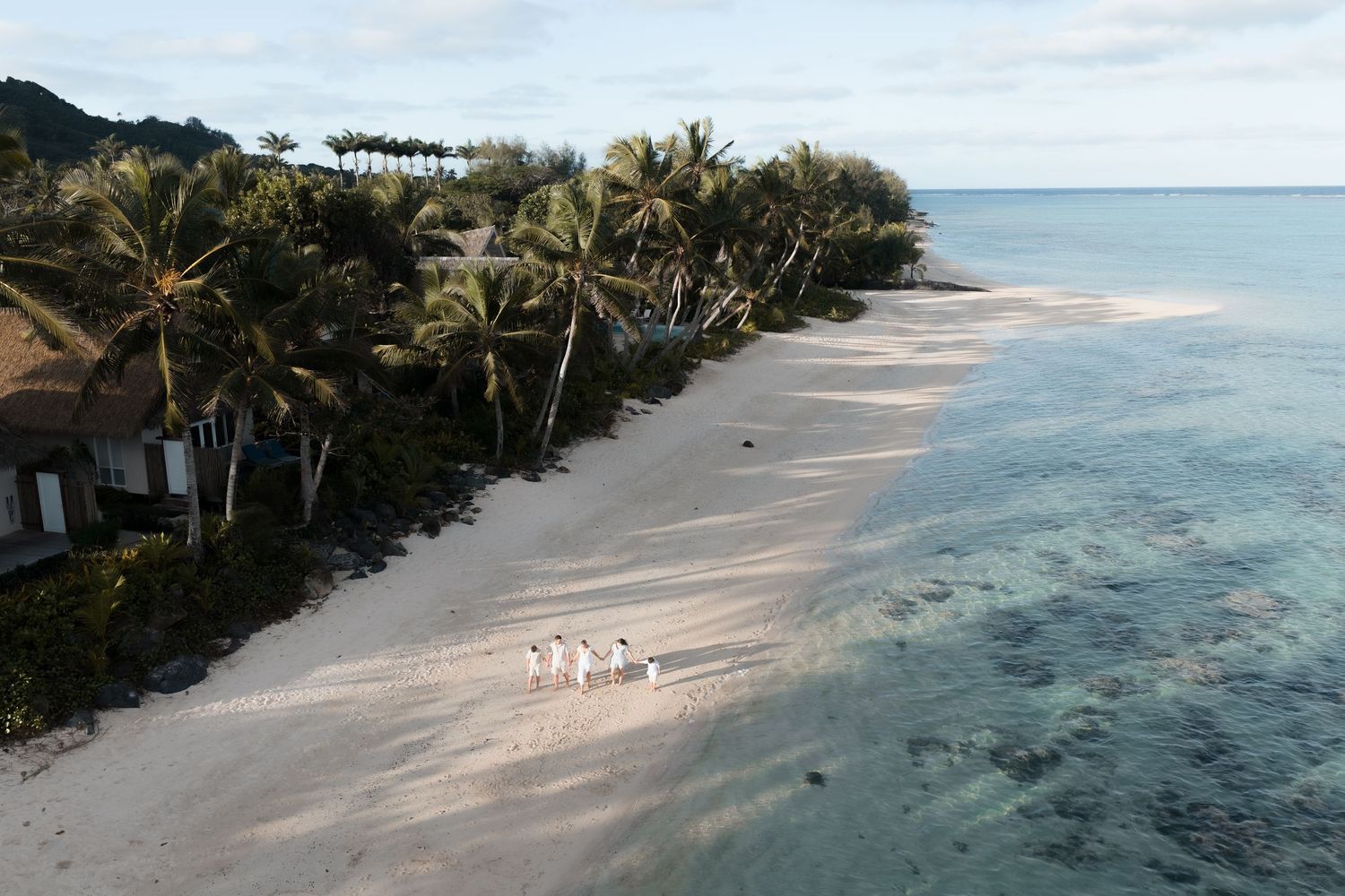 Aerial view of a tropical white sand beach with palm trees, clear turquoise water, and a small group of people walking.