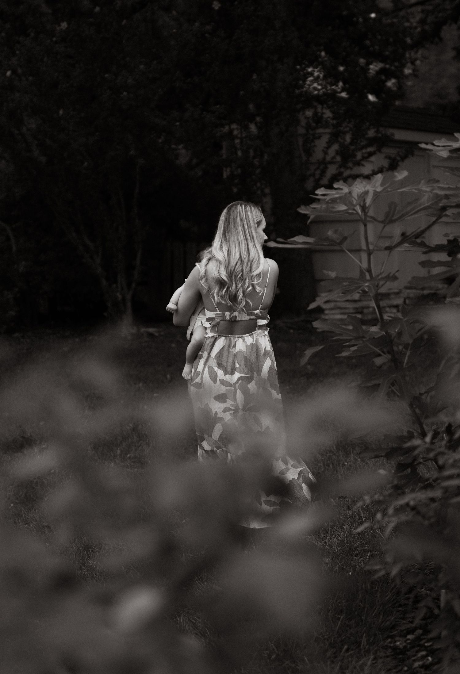 A woman in a vibrant floral maxi dress walks through a lush green garden, her blonde hair flowing down her back.