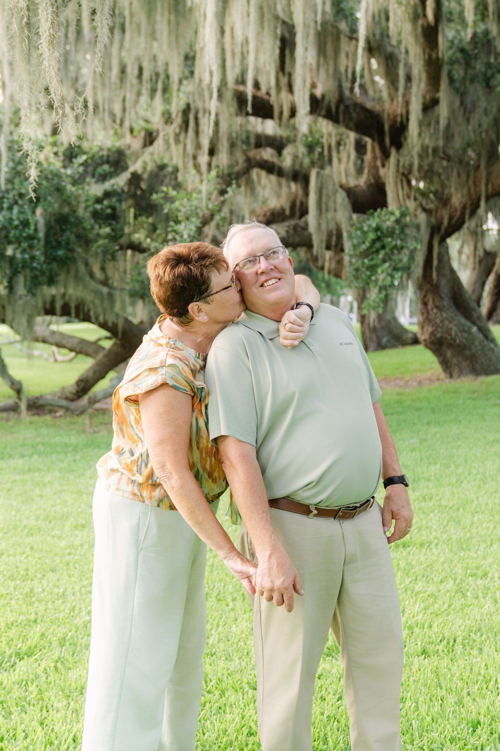 Couple shares a playful moment beneath the oak trees during an anniversary portrait session on Jekyll Island