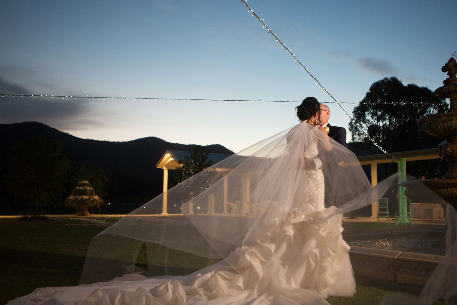 Bride and groom embracing at dusk with a flowing long veil, captured by Norfolk wedding photographer.