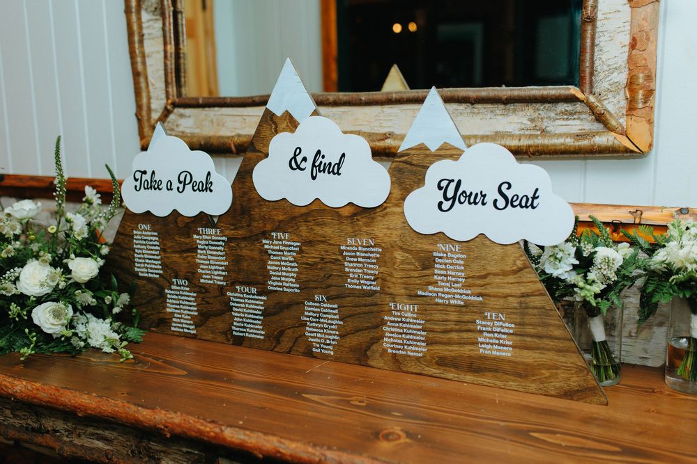 Rustic wooden wedding seating chart with cloud and mountain cutouts reading Take a Peak and Find Your Seat.