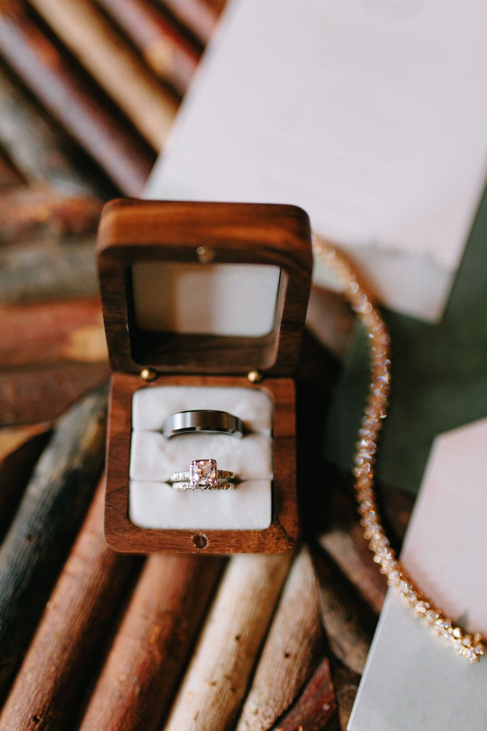 Wedding rings displayed in wooden ring box with pearl necklace on rustic wooden background.