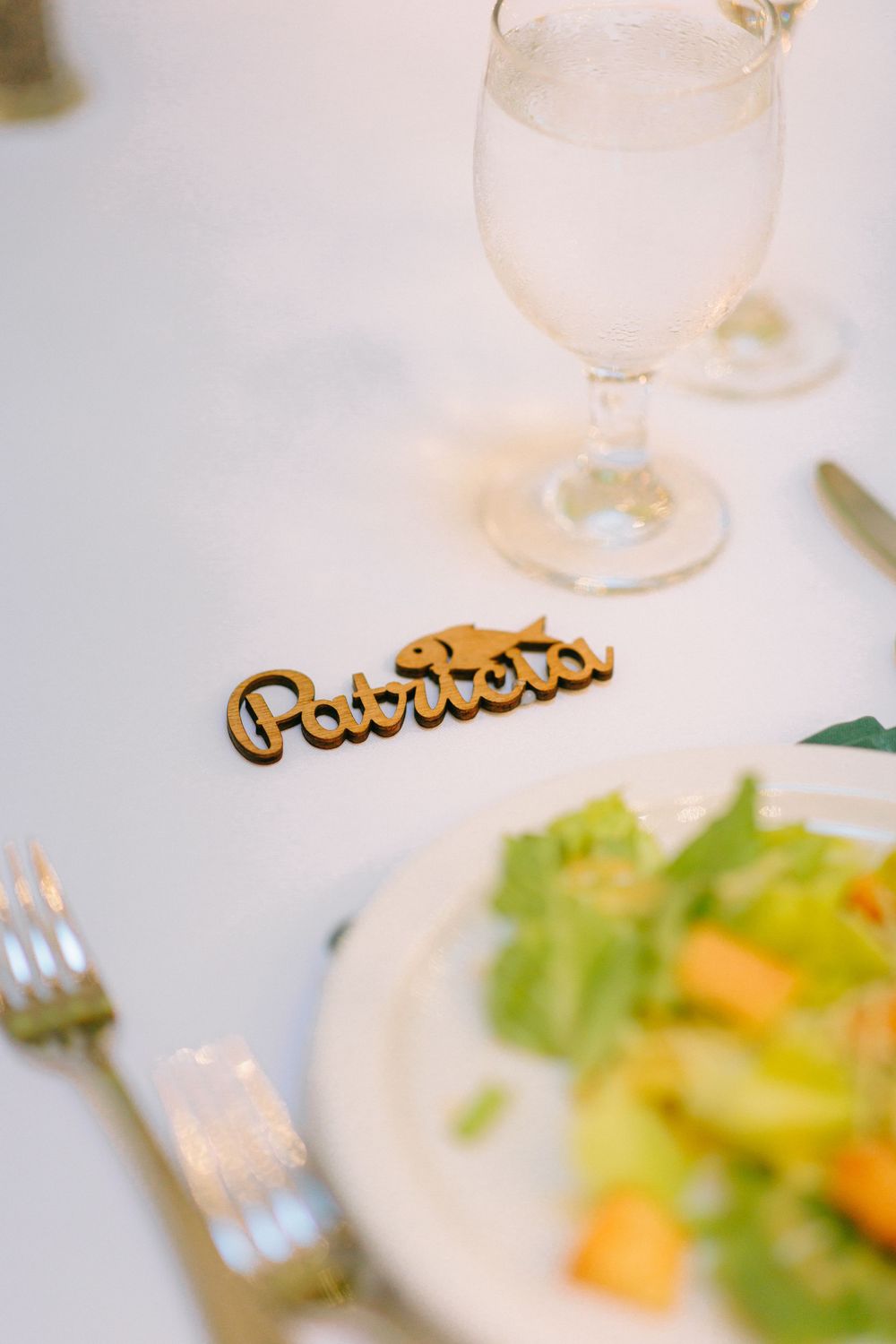 Gold Patriots laser cut place card on white wedding reception table with salad plate and glass.