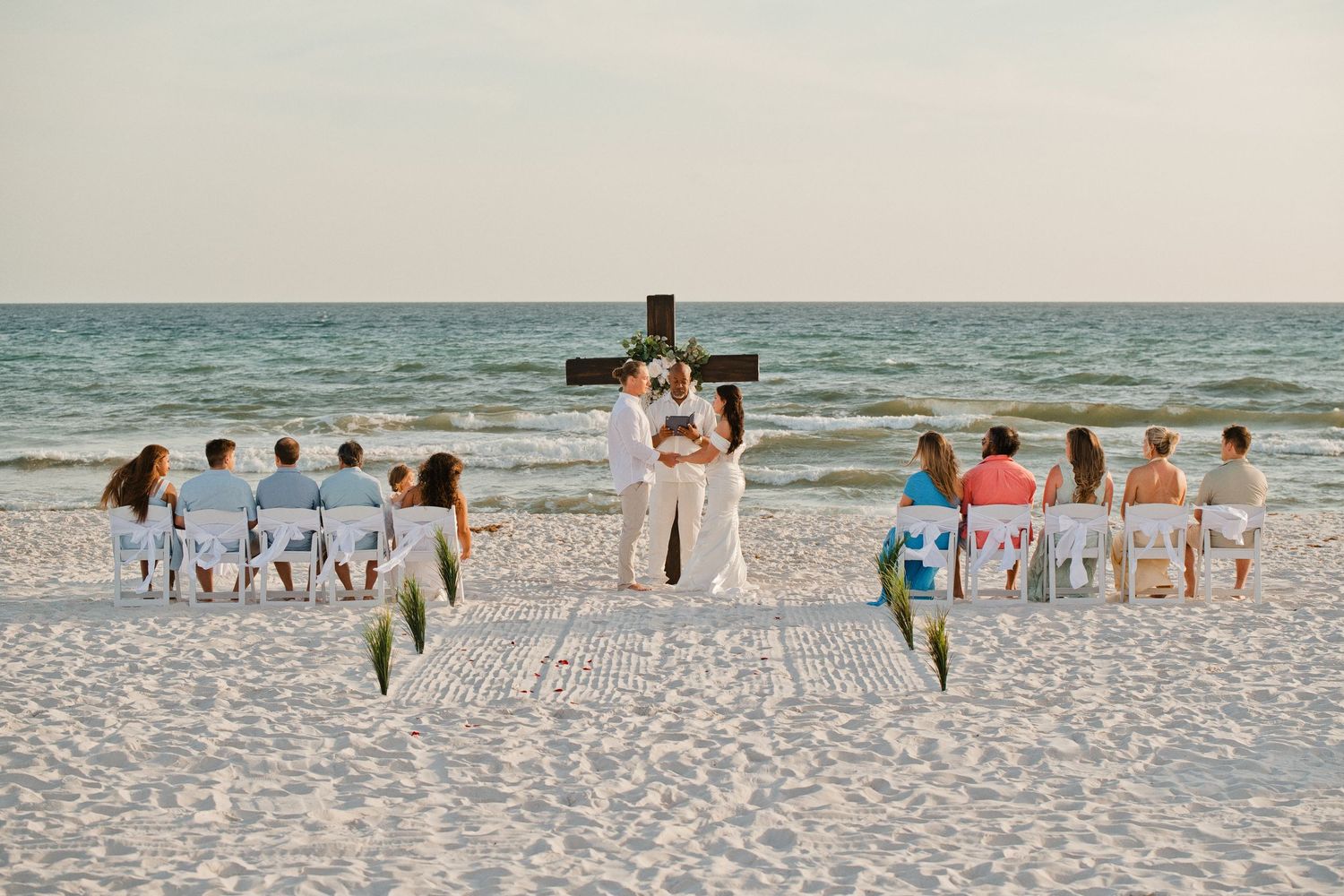 Family of eight poses together on a sandy beach at sunset, dressed in coordinating neutral and white outfits.