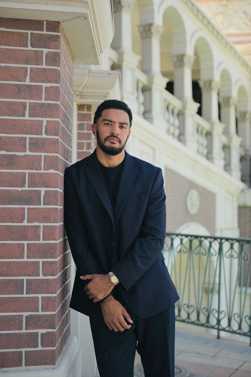 Businessman in dark suit posing by brick column at elegant venue.