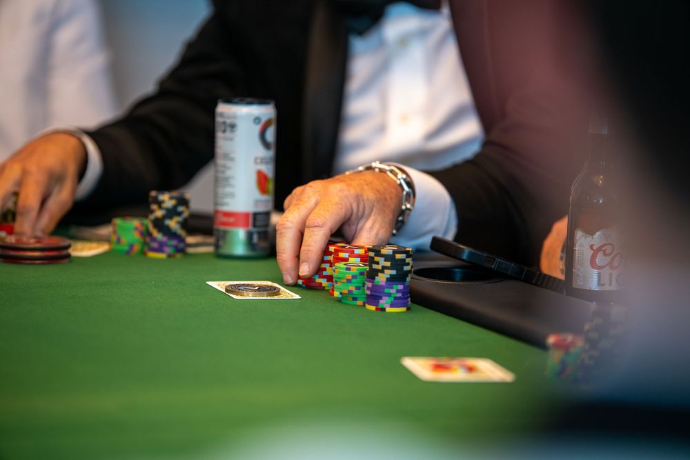 Players at a casino poker table with colorful chips stacked on green felt during an intense card game.