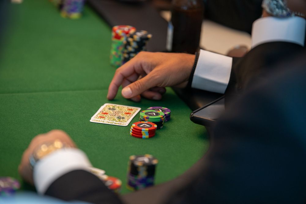 Close-up of poker players at a casino table with chips and playing cards on green felt.