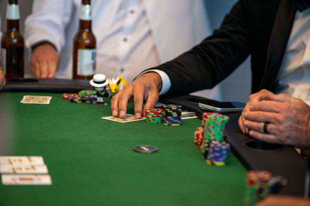 Players gather around a green felt poker table with colorful casino chips and cards during a high-stakes card game.