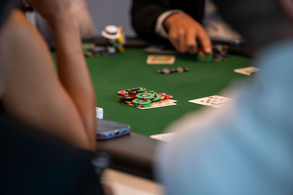 Players gathered around a green felt poker table with colorful casino chips and playing cards during a card game.