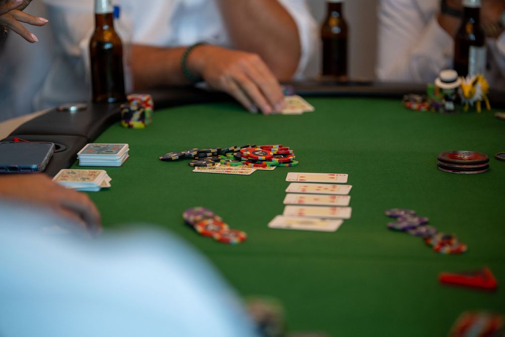 Players gathered around a green felt poker table with cards and colorful casino chips during a card game.