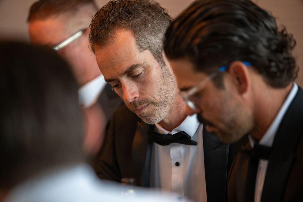 Men in tuxedos with bow ties gathered closely together at a formal event or wedding ceremony.