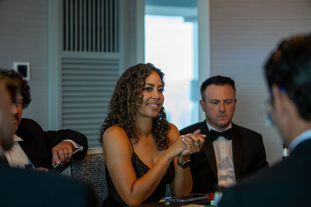 Woman with curly hair smiling and clapping at a formal casino night event.