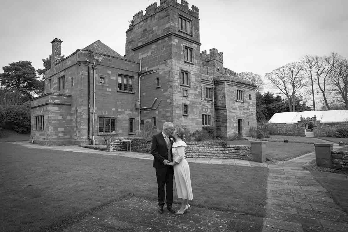Couple embracing in front of a historic stone manor house in a black and white wedding portrait.