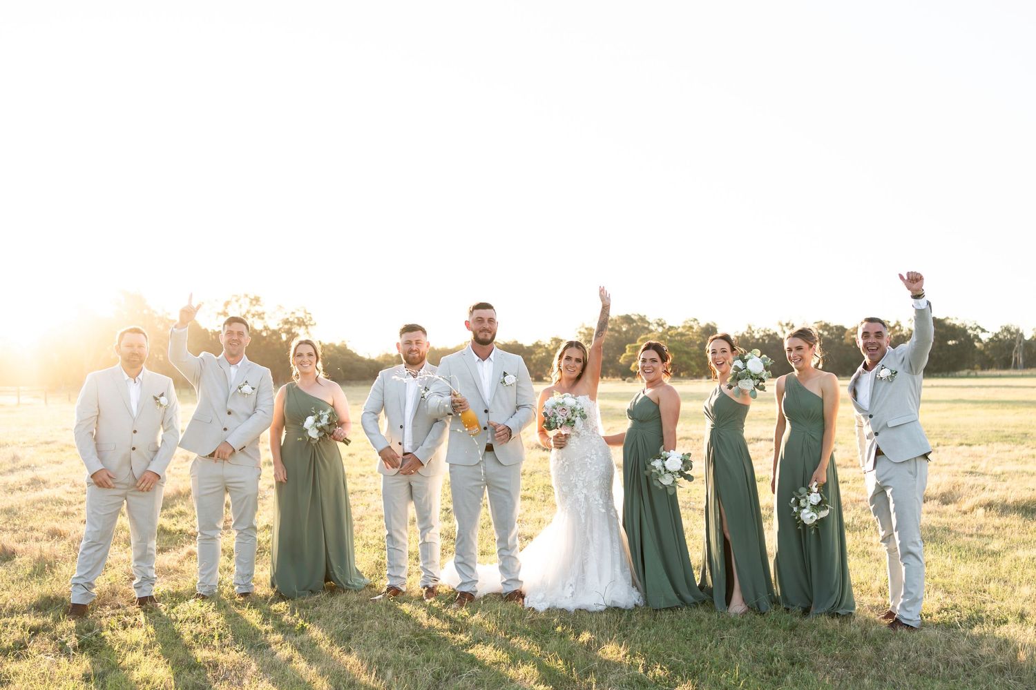 A romantic couple shares a kiss in a sunlit field, the bride wearing a flowing lace gown and the groom in a light gray suit.