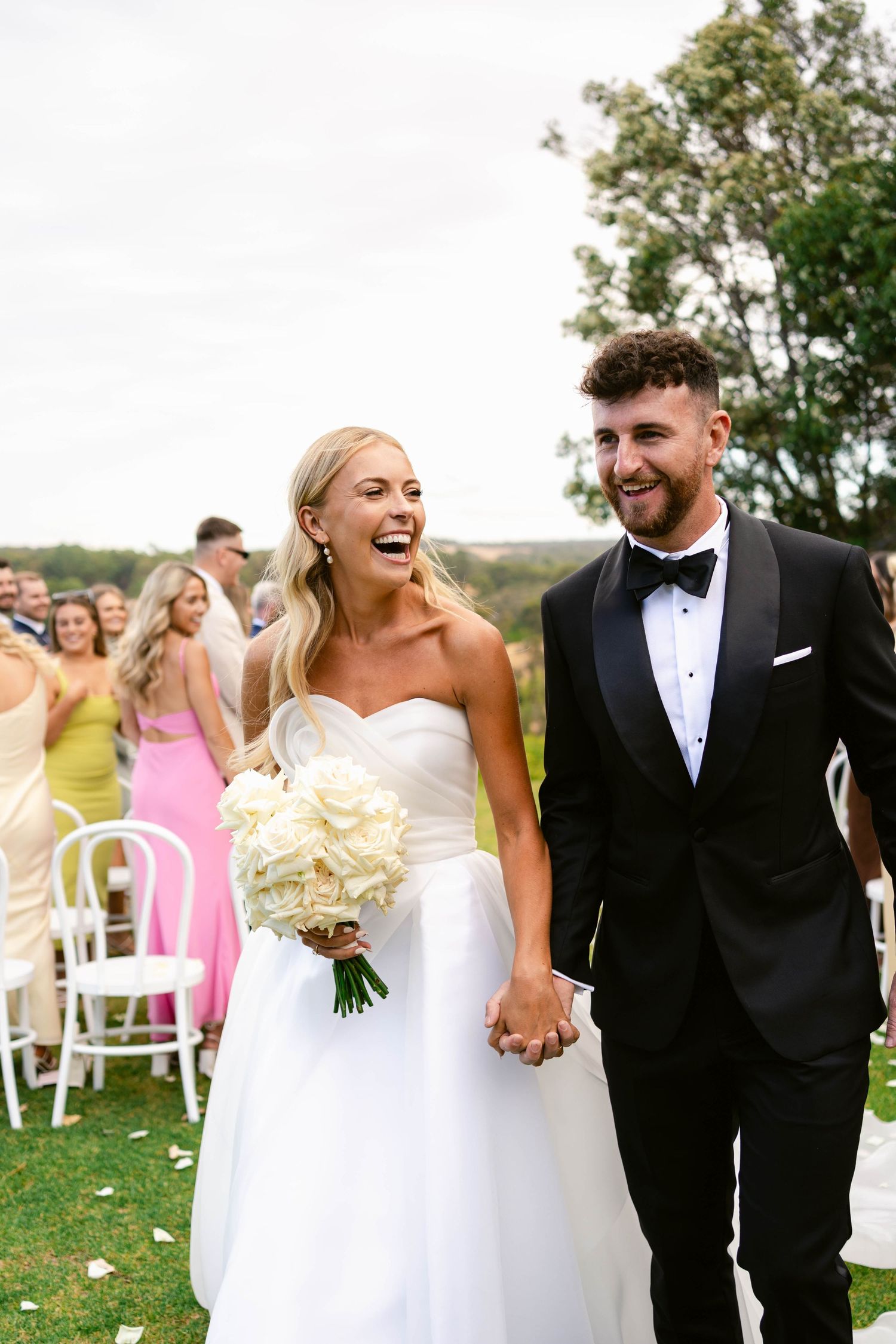 Black and white photo sequence showing a couple in wedding attire dancing playfully on a grassy hillside.