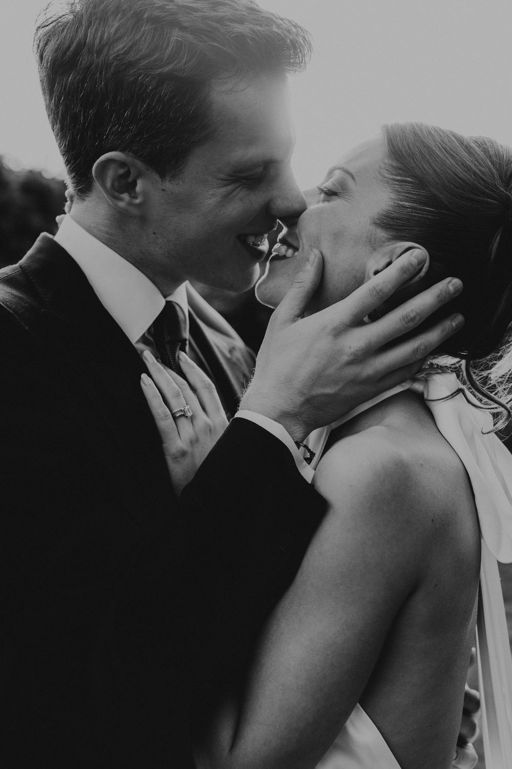 Black and white photo of a groom tenderly holding his bride's face as they share a romantic kiss on their wedding day.