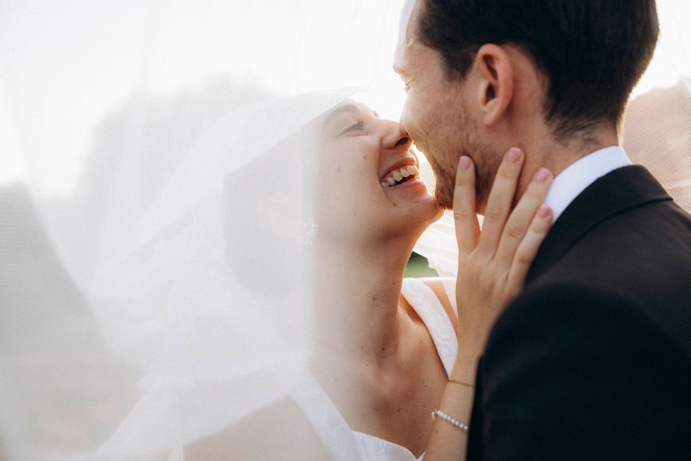Joyful bride and groom sharing a romantic moment, with flowing veil and elegant wedding attire.