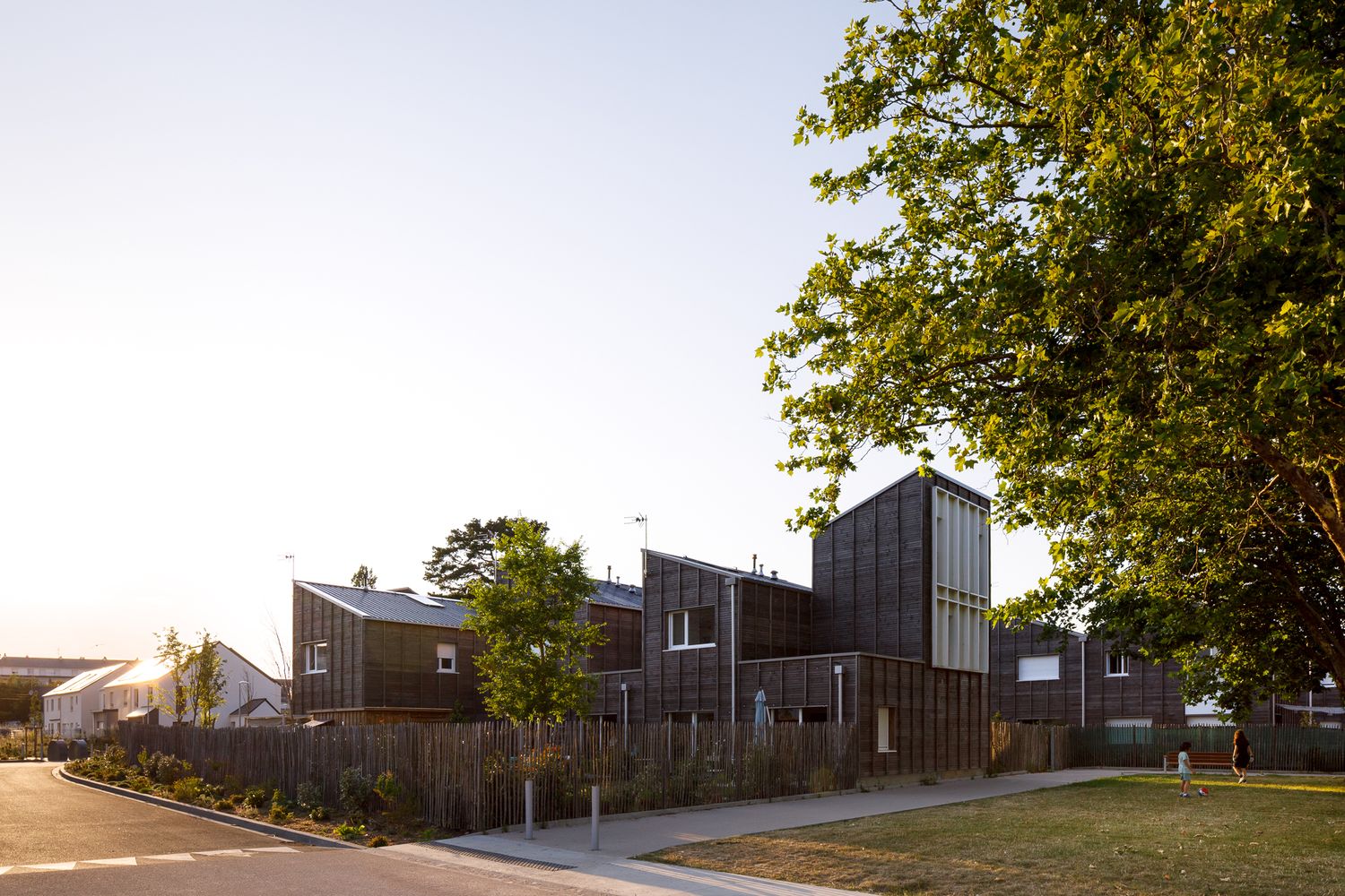 Alignement de maisons contemporaines avec bardage en bois sombre au coucher du soleil, photographié par Damien Sebök à Saint-Nazaire.