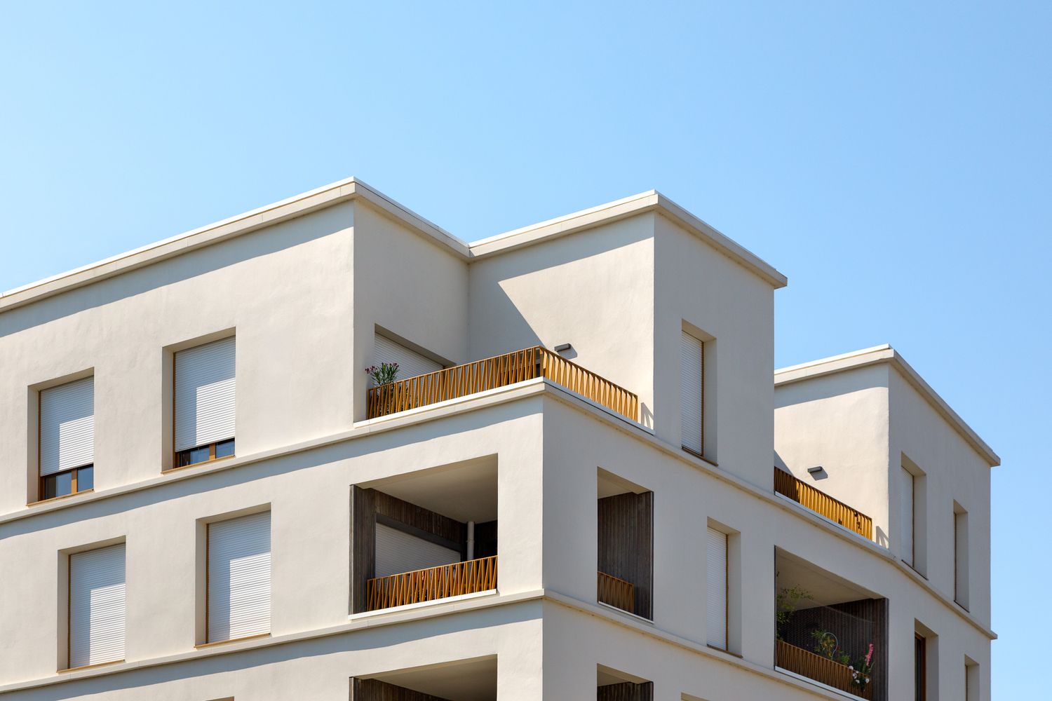 Immeuble d'appartements contemporain couleur crème, avec balcons en gradins et balustrades en bois chaleureux, se détachant sur un ciel bleu