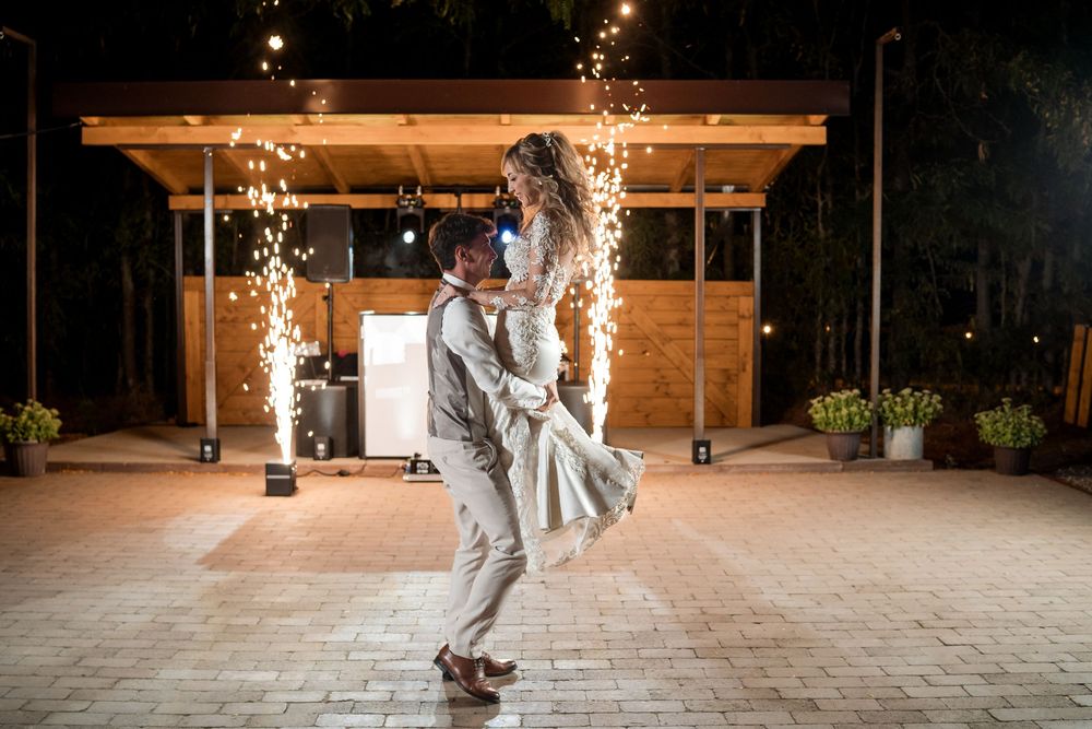 Bride and groom share romantic first dance outdoors at night with sparkling fireworks fountain backdrop at wedding reception.