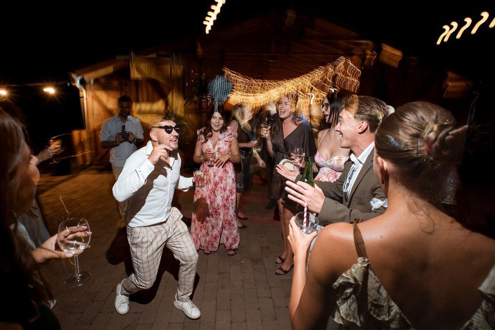 Guests dancing and celebrating at an outdoor wedding reception under warm string lights at night.