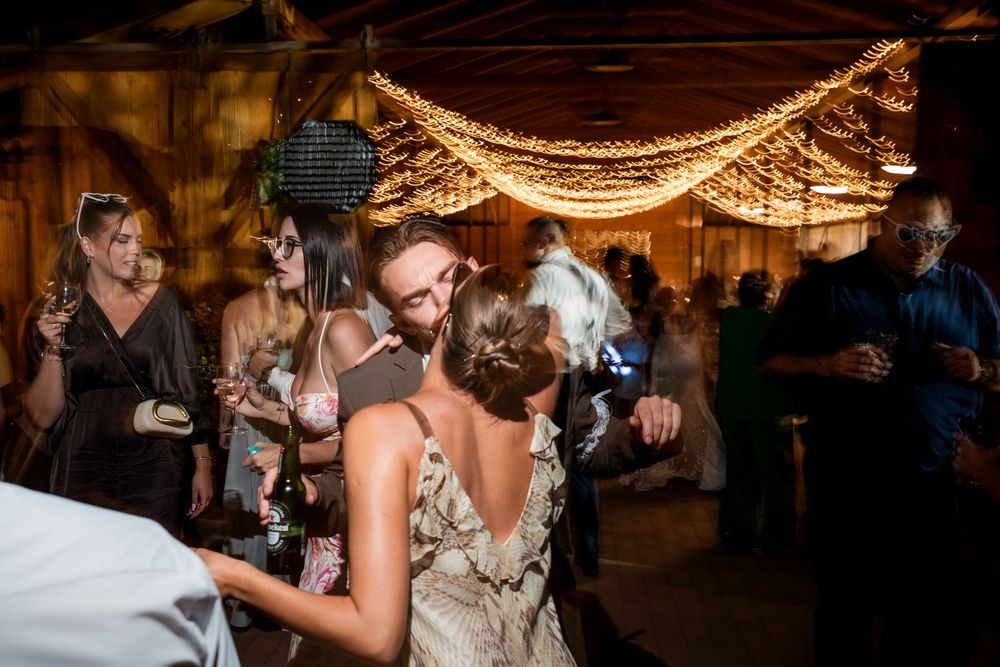 Bride and guests dancing under warm string lights at an elegant indoor wedding reception celebration.