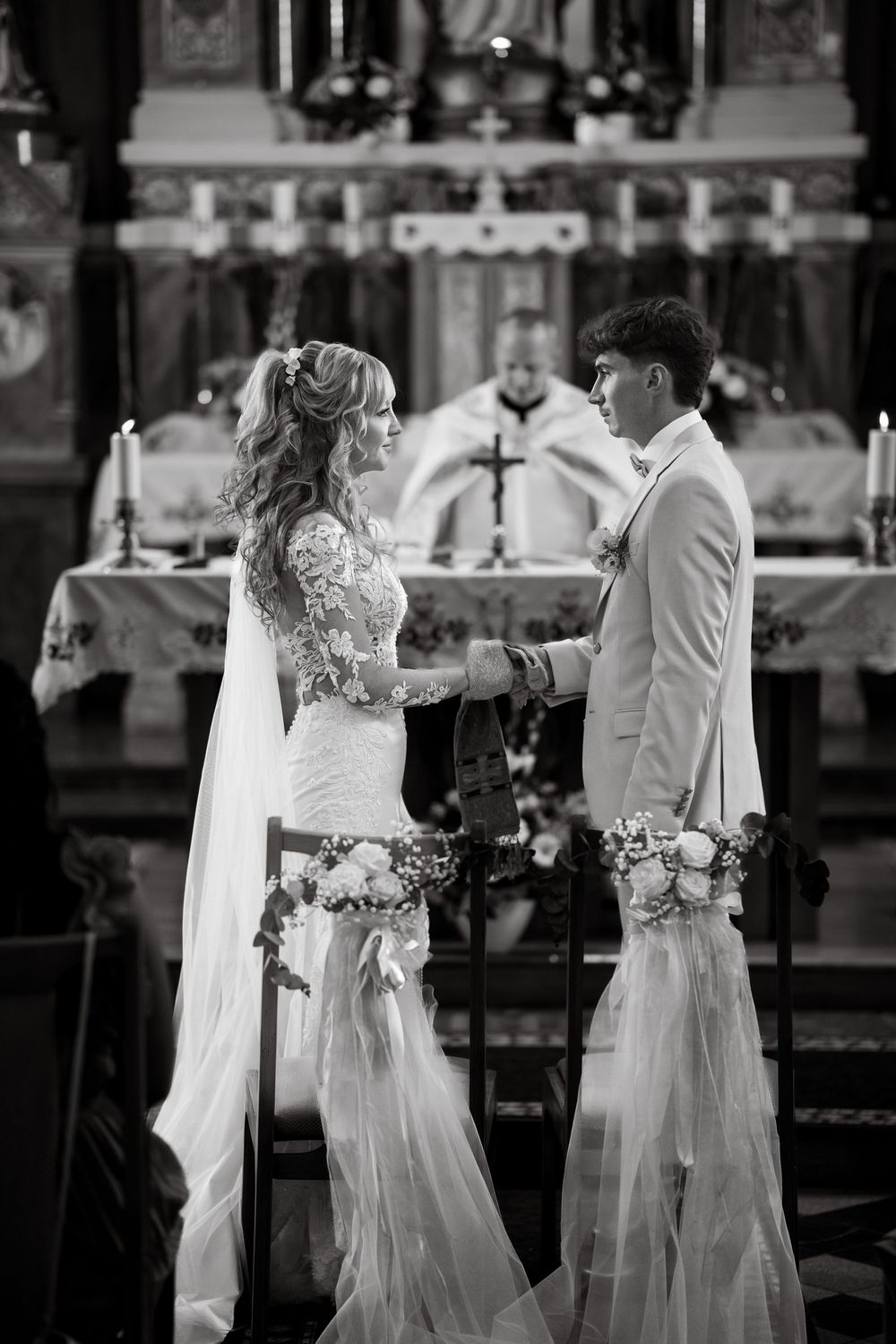 Black and white photo of bride and groom exchanging vows at church altar during wedding ceremony.