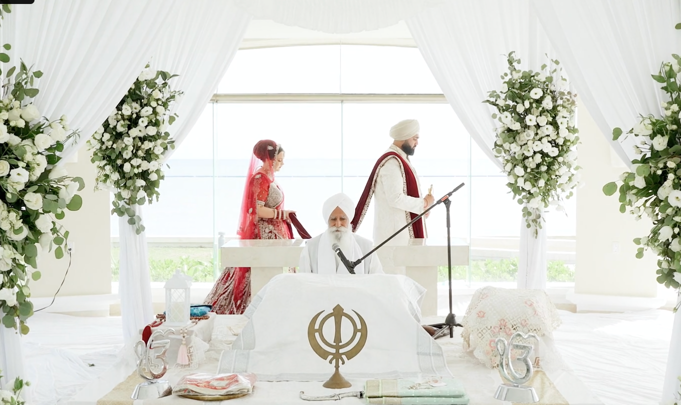 Sikh wedding ceremony couple standing at white floral altar during traditional Anand Karaj marriage ritual.