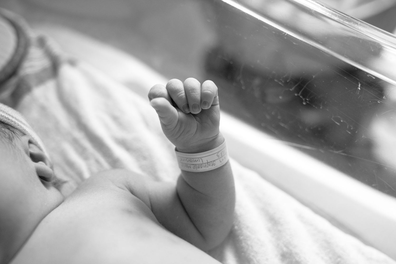 Black and white photo of a newborn baby hand with hospital ID bracelet in a hospital nursery.