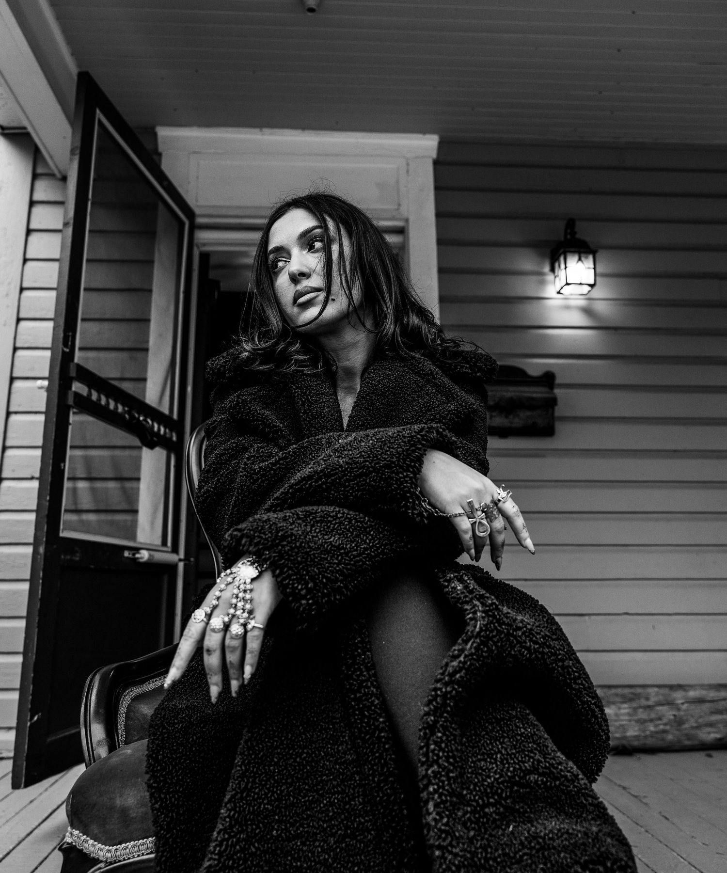 Woman in black fluffy coat poses on porch at night, black and white portrait photography.