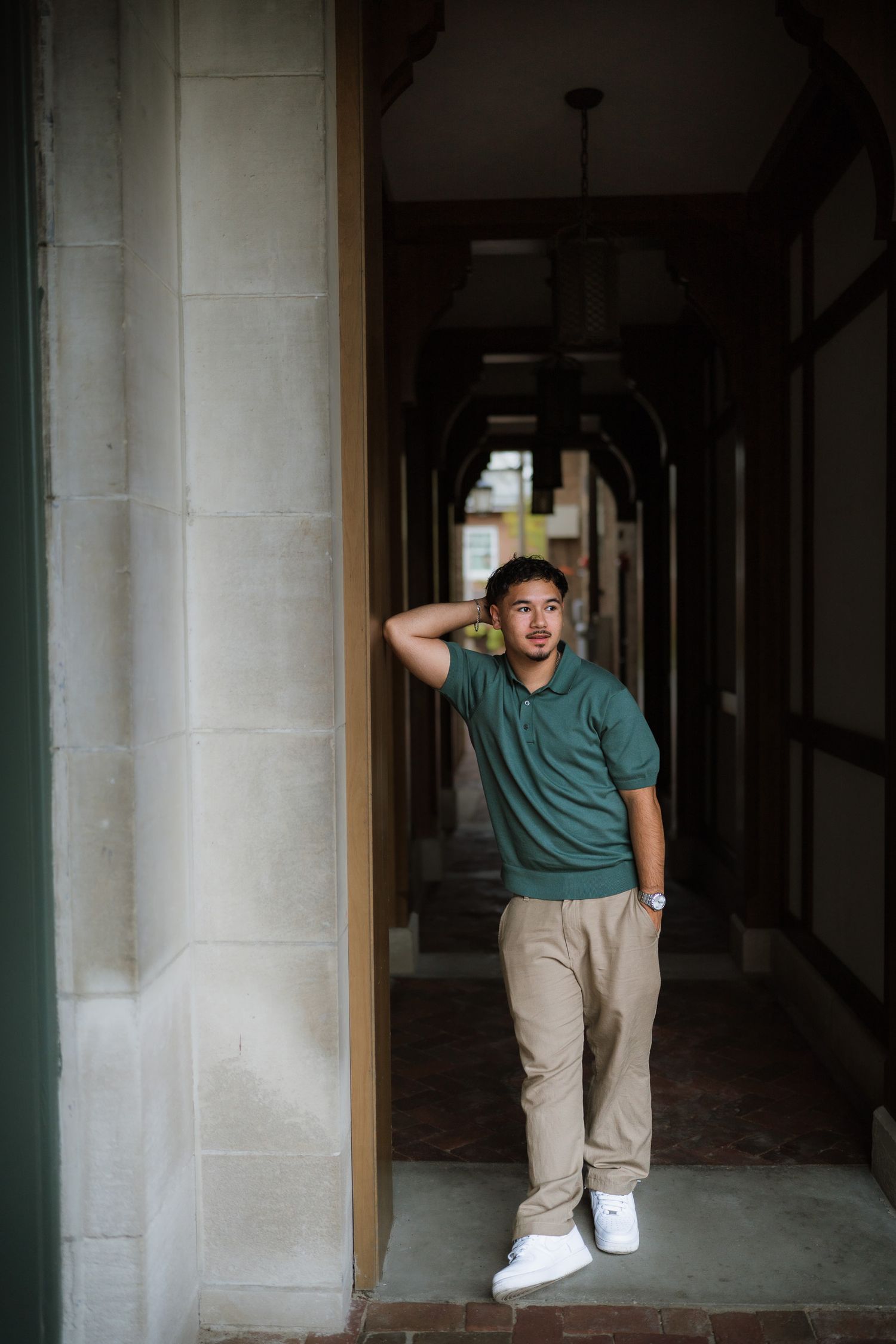Young man in green polo and khaki pants poses in an elegant stone archway corridor.