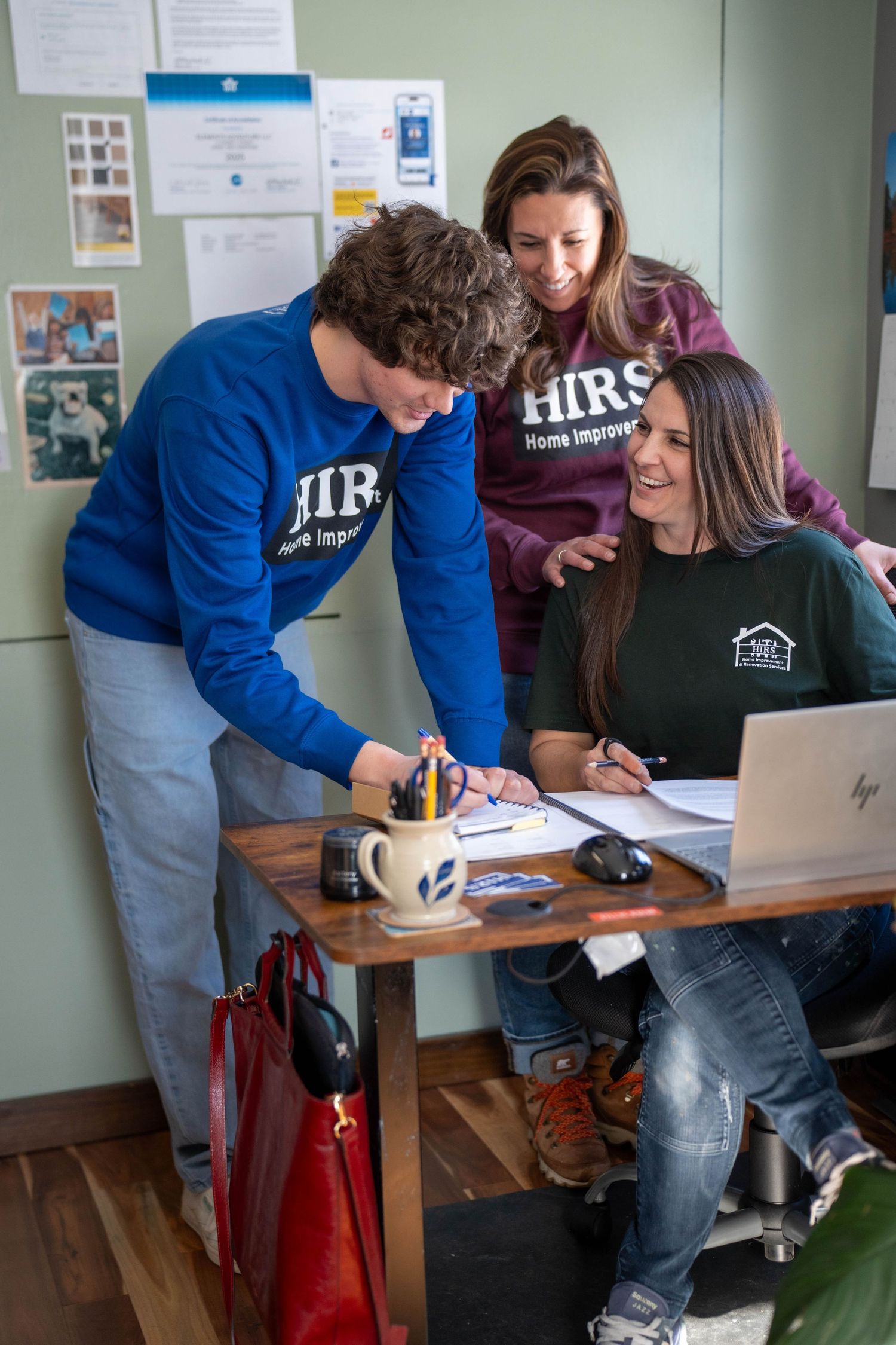 Three HIRS Home Improvement team members collaborating over documents and a laptop at an office desk.