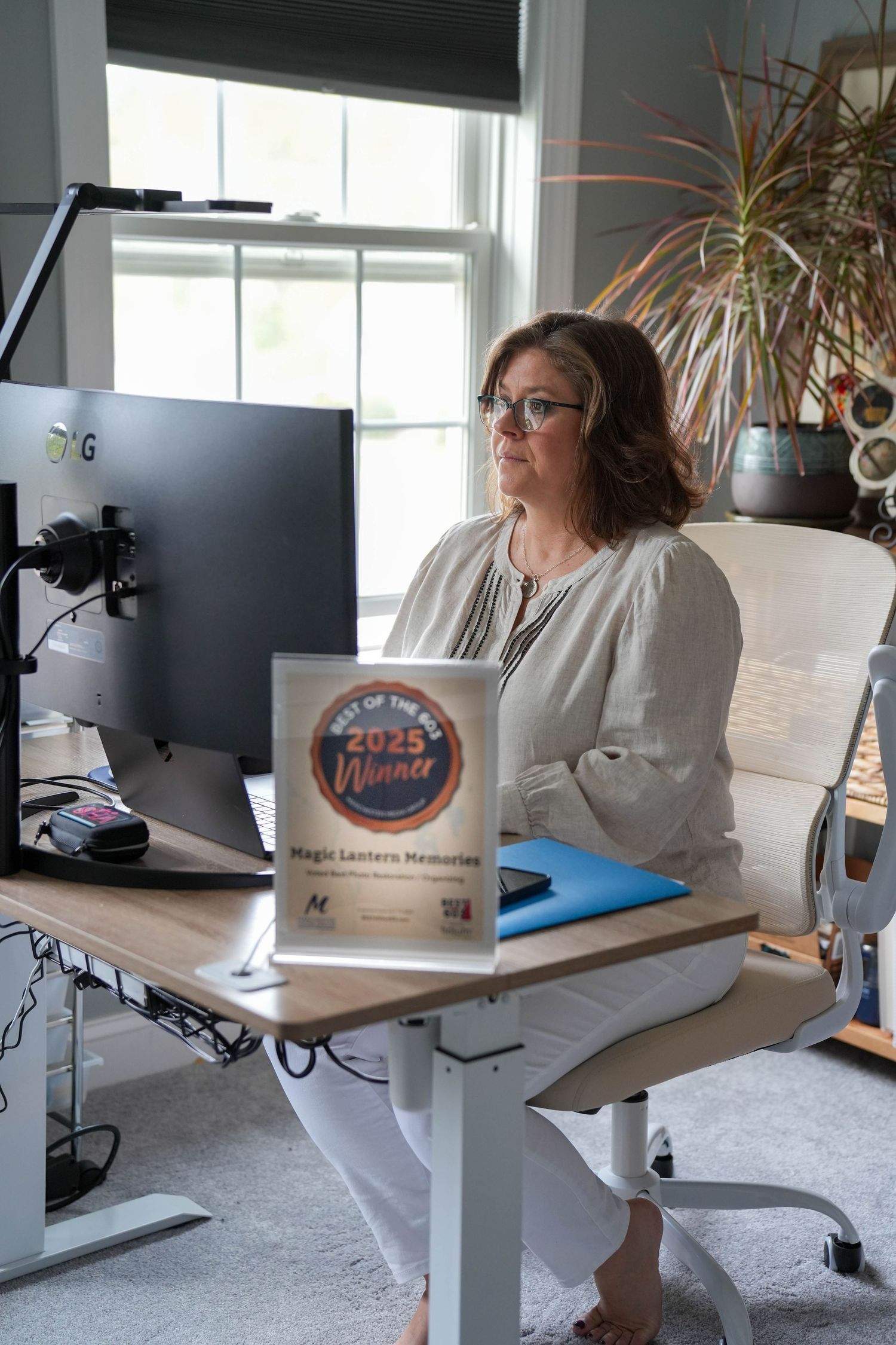 Woman sitting at a standing desk with a 2025 Best of the Year Winner award for Magic Lantern Memories.