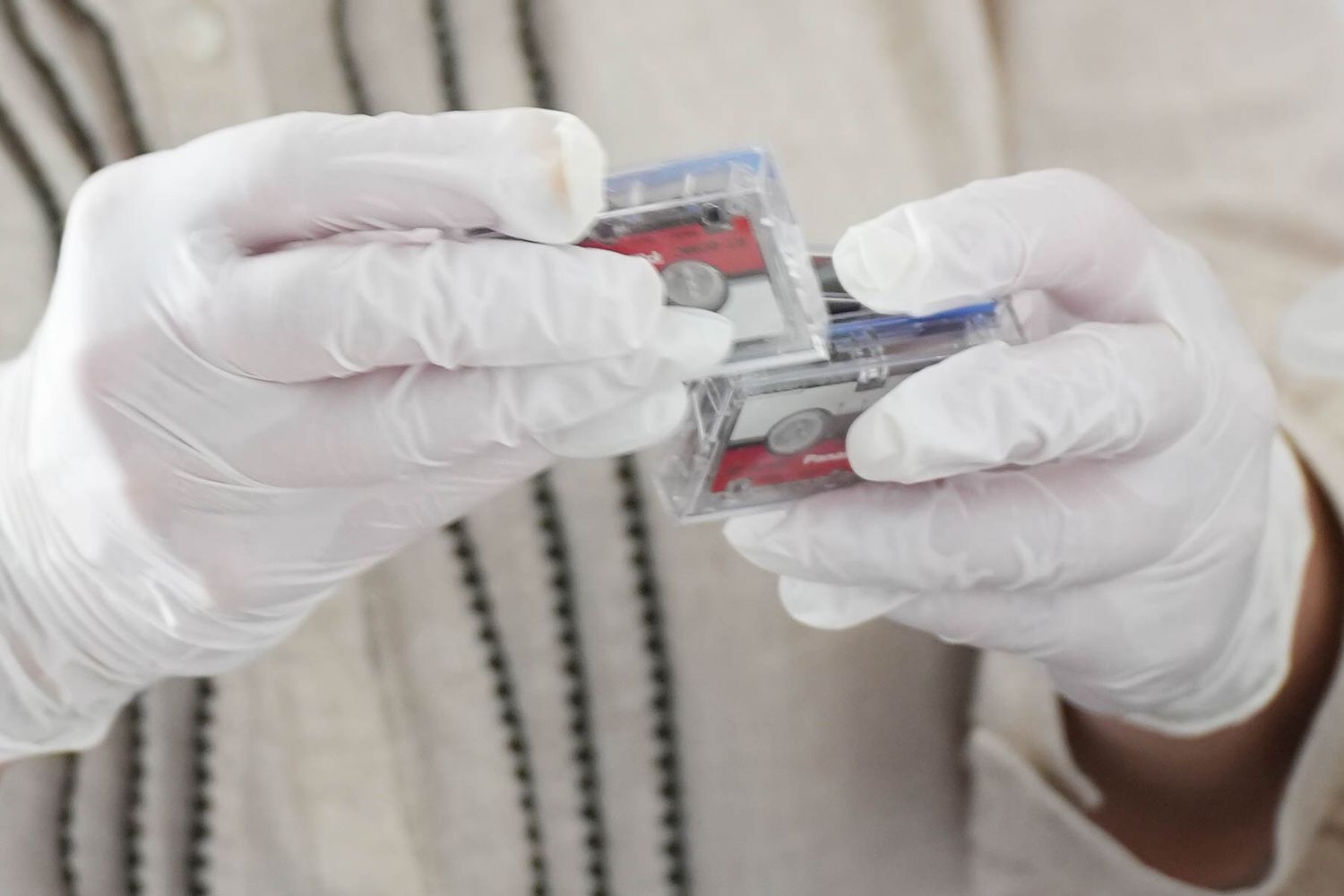 Gloved hands carefully handling a medical test cartridge or diagnostic device in a laboratory setting.