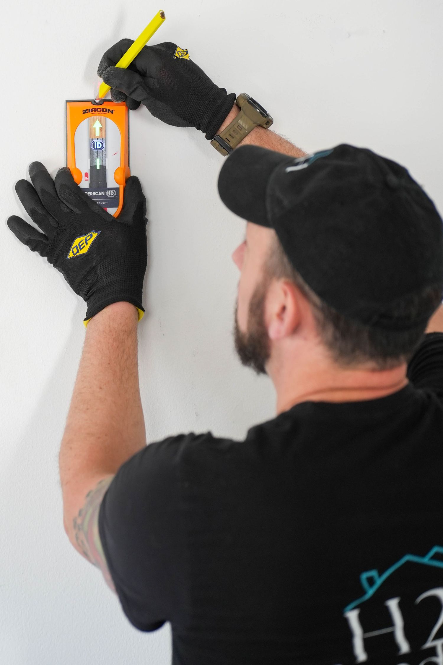 Worker in black gloves and cap uses a level tool to mark measurements on a white wall.