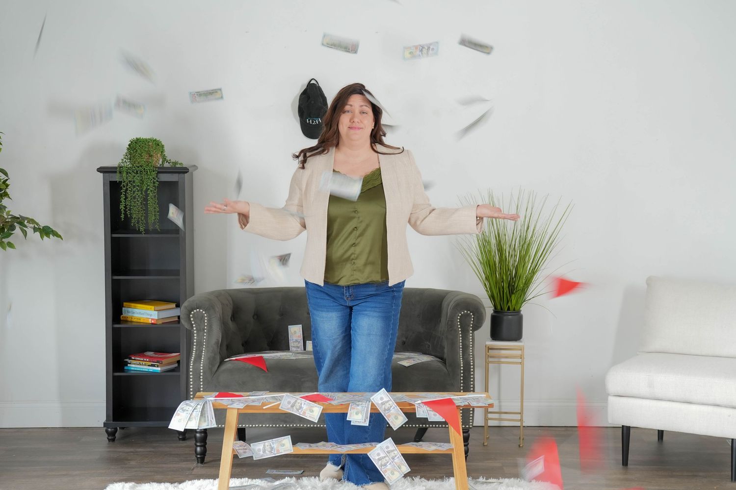 Woman joyfully tossing papers in air in modern living room with sofa, bookshelf, and scattered documents on coffee table.