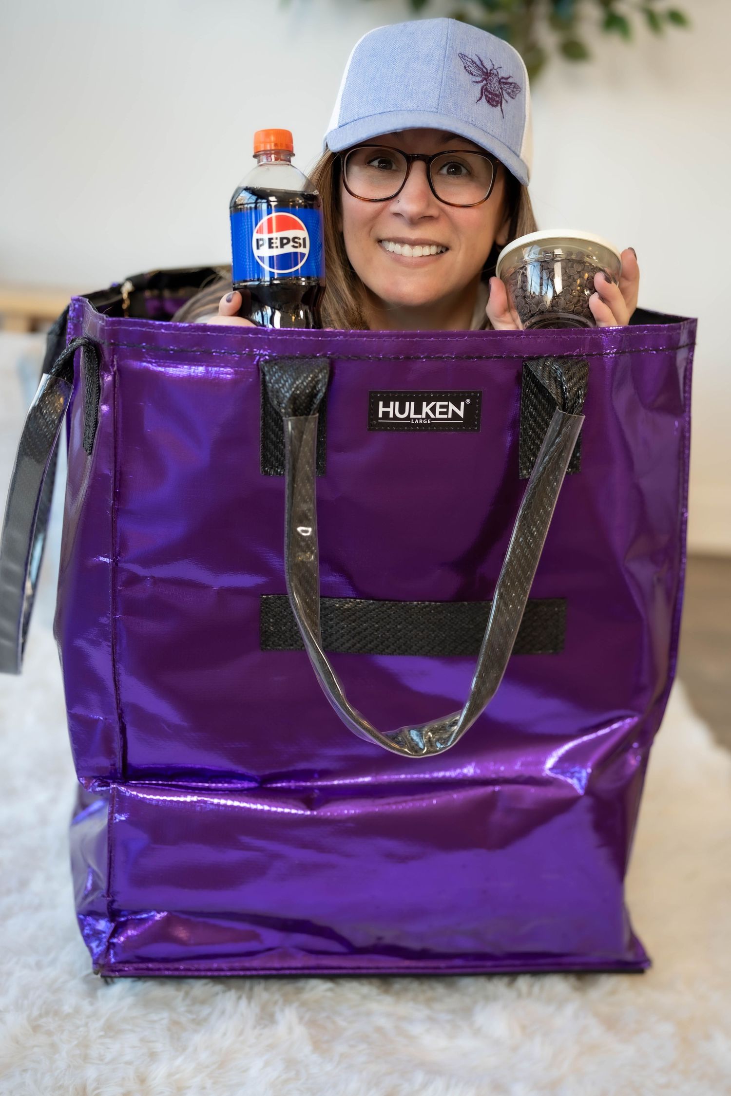 Woman smiling behind a purple Hulken tote bag containing a Pepsi bottle and a clear cup.
