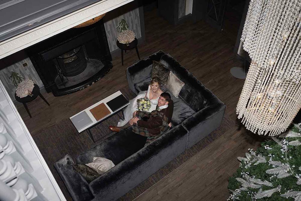 Aerial view of a bride sitting on a gray velvet sofa in an elegant living room with chandelier.
