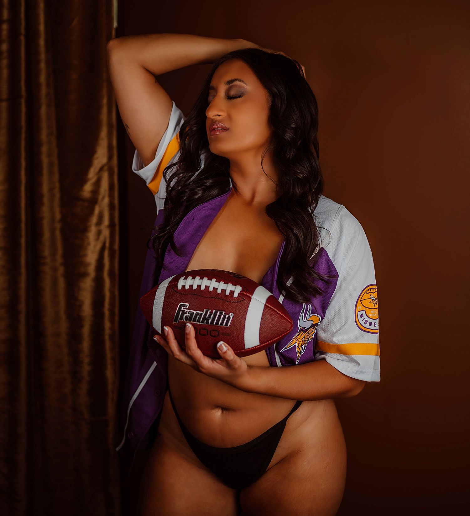 woman holds football in open jersey for sporty boudoir session