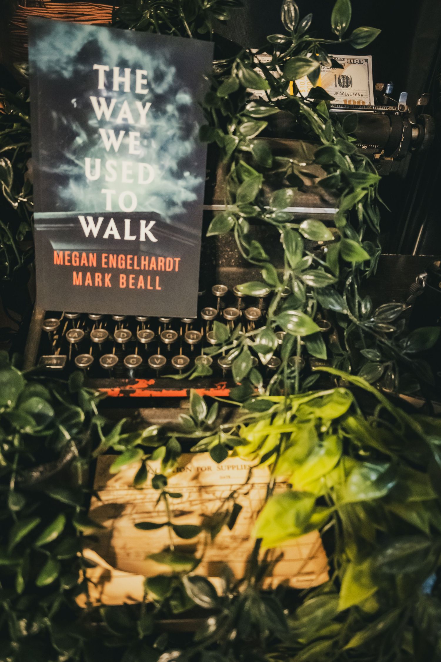 Book 'The Way We Used to Walk' by Megan Engelhardt and Mark Beall displayed beside a vintage typewriter with lush green plants.